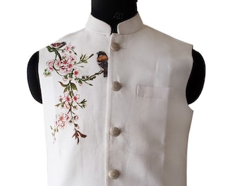 May include: White vest with a mandarin collar and a bird and floral design. The sleeveless vest has a button-up front with four silver buttons and two front pockets. The bird is perched on a branch with pink flowers.