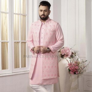 Puede incluir: Un traje kurta rosa claro con un chaleco bordado a juego y pantalones blancos. El conjunto presenta un cuello mandar&iacute;n y se combina con mocasines de cuero marr&oacute;n. El texto "PARIVAR CEREMONY" es visible.