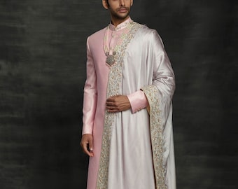 Puede incluir: Un atuendo formal rosa y blanco. La chaqueta de manga larga tiene cuello mandarín y se combina con pantalones blancos y una bufanda a juego. La bufanda está drapeada sobre el hombro y tiene un borde bordado. Un collar de cuentas y zapatos rosas completan el look.