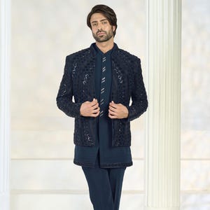 Puede incluir: Un traje formal azul marino con una chaqueta texturizada con detalles intrincados, una camisa a juego y pantalones a medida. El conjunto se completa con zapatos azul marino. El atuendo est&aacute; dise&ntilde;ado para una apariencia sofisticada y elegante.