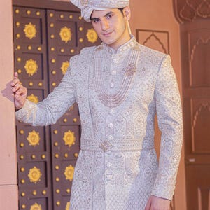 May include: A light blue embroidered sherwani with a matching turban. The sherwani features intricate patterns, a pearl necklace, and a decorative belt. The outfit is worn with a matching turban, creating a formal and elegant look.