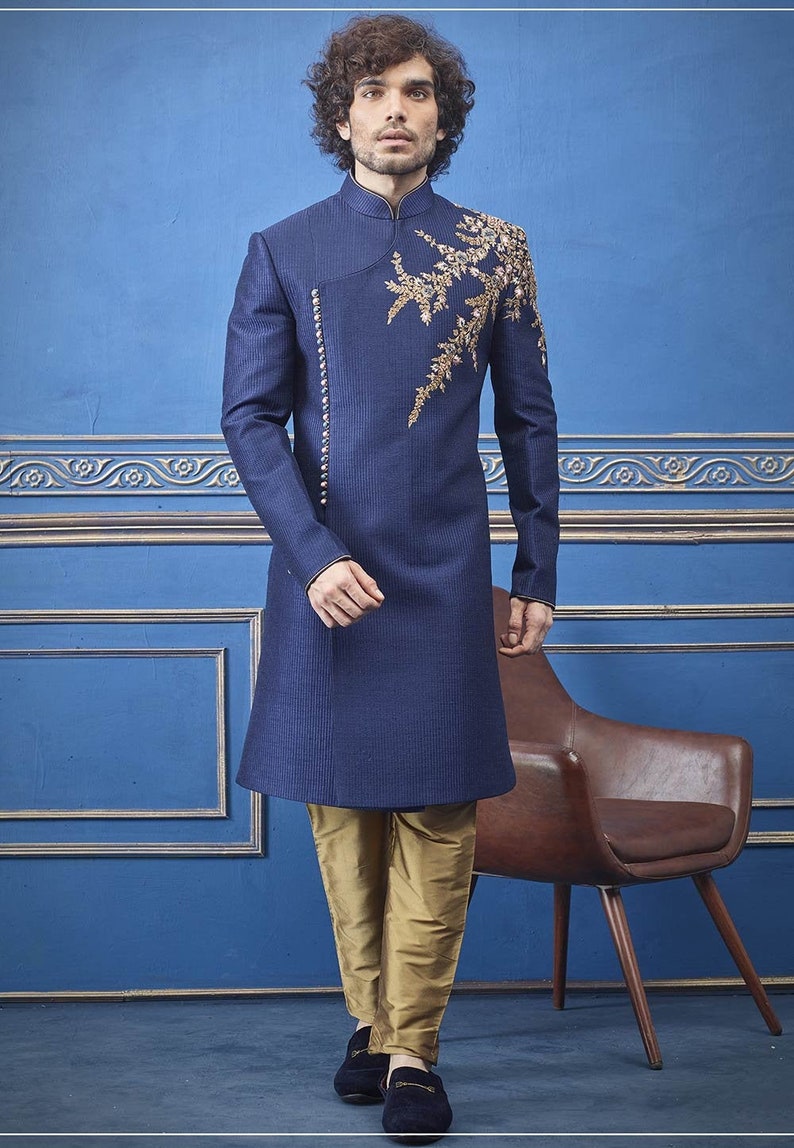 Puede incluir: Una kurta azul marino de manga larga con bordados dorados en el pecho. La kurta se combina con pantalones dorados y zapatos negros.