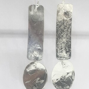 May include: Silver dangle earrings with a textured rectangular charm and a round charm with an engraved hummingbird design.
