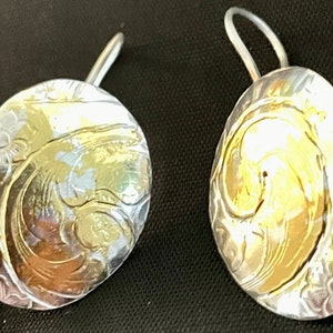 Peut inclure: Une paire de boucles d'oreilles en argent avec un motif en spirale doré. Les boucles d'oreilles sont rondes et ont une surface texturée.