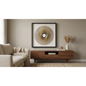 May include: A square wall art piece featuring a circular, sunburst-like design made of fine, radiating beige and gold threads centered around a small, reflective circular mirror, all enclosed within a simple, thin black frame.