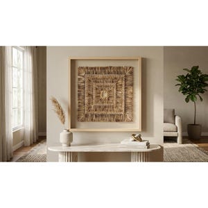 May include: A square wall art piece featuring a textured, woven natural fiber design in shades of tan and brown, encased in a light-colored wooden frame. The artwork displays a concentric square pattern with a small open center square.
