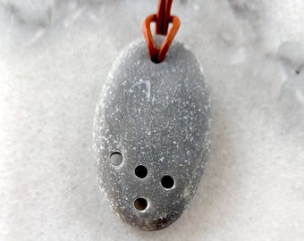 May include: A gray stone pendant with four holes, hanging from a brown leather cord.