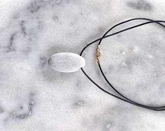 May include: A white oval stone pendant on a black cord necklace.