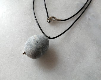 May include: A gray stone pendant necklace with a black leather cord. The stone is smooth and oval-shaped.