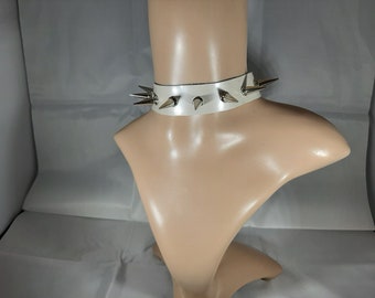 May include: White leather choker with silver spikes. The choker is on a mannequin's neck.