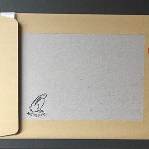May include: A brown paper envelope with a white flap. The envelope has a gray inner lining with a black and white illustration of a rabbit and the text "Artful Hare". The envelope has a red recycling symbol in the upper right corner.