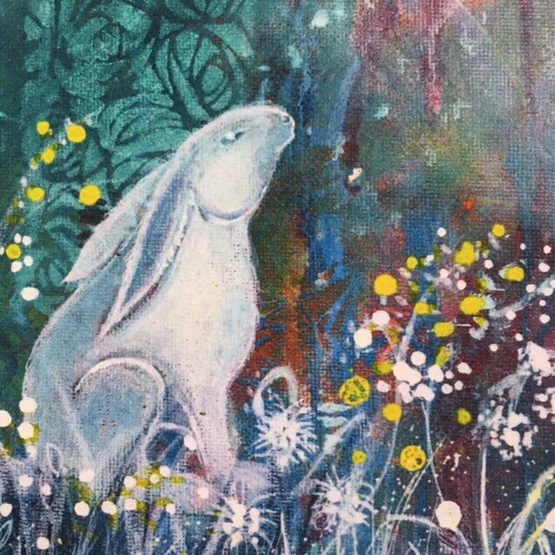 May include: A white rabbit sits in a field of white and yellow flowers. The background is a blur of green and blue.
