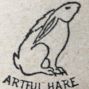 May include: A black and white line drawing of a rabbit sitting up with its ears perked up. The text "Artful Hare" is written below the rabbit.