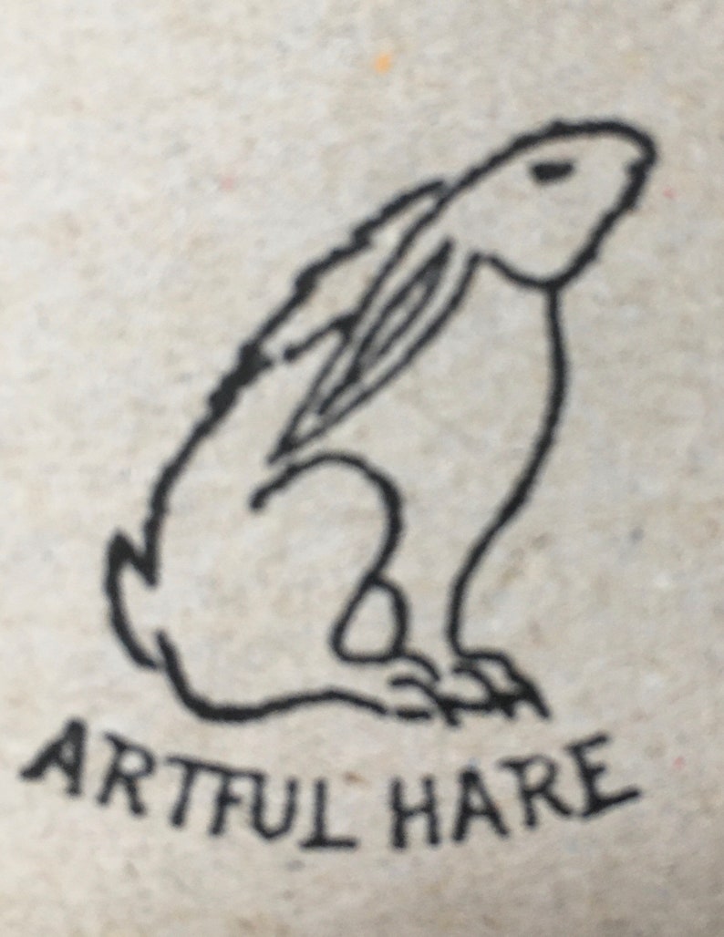 May include: A black and white line drawing of a rabbit sitting up with its ears perked up. The text "Artful Hare" is written below the rabbit.