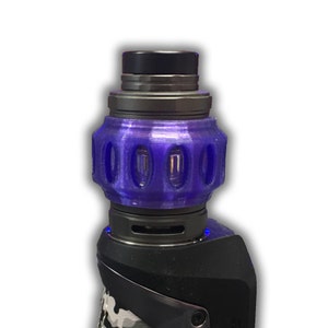 May include: A purple vape tank with a black top and a clear glass section. The tank has a unique design with multiple holes around the middle.