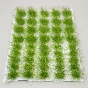 May include: A sheet of miniature, bright green grass tufts, arranged in neat rows. The artificial grass has a textured, realistic appearance, perfect for model landscapes or craft projects. The grass is attached to a white backing.