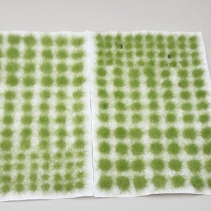 May include: Two sheets of green static grass tufts, each sheet has 100 tufts arranged in a grid pattern. The tufts are a light green color and are attached to a white backing.