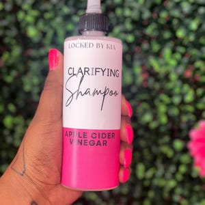 May include: A pink bottle of clarifying shampoo with a black cap and a white label that says "LOCKED BY KIA" and "CLARIFYING Shampoo APPLE CIDER VINEGAR".