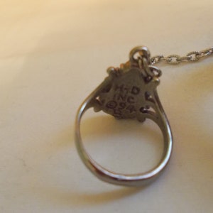 May include: A silver ring with a decorative design and a chain attached. The ring has the inscription "HTD INC 924" on the back.