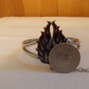 May include: Silver bracelet with a black and white flame design. The bracelet has a chain attached to it. A US quarter is included for size reference.