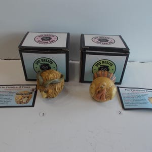 May include: Two small ceramic figurines of a turkey and a ram, both with brown, tan, and green paint. The figurines are part of a collection called "Pot Bellys" and are labeled "The Farmyard Times".