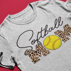 May include: Gray t-shirt with the text "Softball Mom" in black script. The "Mom" is in leopard print with a yellow softball in the center.