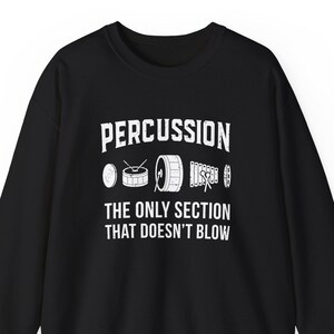 Può includere: Felpa nera con la scritta bianca "PERCUSSION THE ONLY SECTION THAT DOESN'T BLOW". Il design include illustrazioni di vari strumenti a percussione. Felpa girocollo.