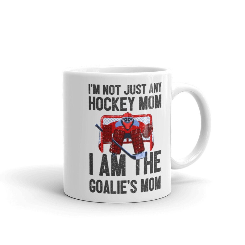 May include: White ceramic coffee mug with a black graphic that reads "I'm not just any hockey mom I am the goalie's mom". The graphic also includes a cartoon image of a hockey goalie in a red and blue uniform.