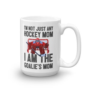 May include: White ceramic coffee mug with a black and white graphic of a hockey goalie in a red and black uniform. The text on the mug reads "I'm not just any hockey mom I am the goalie's mom."