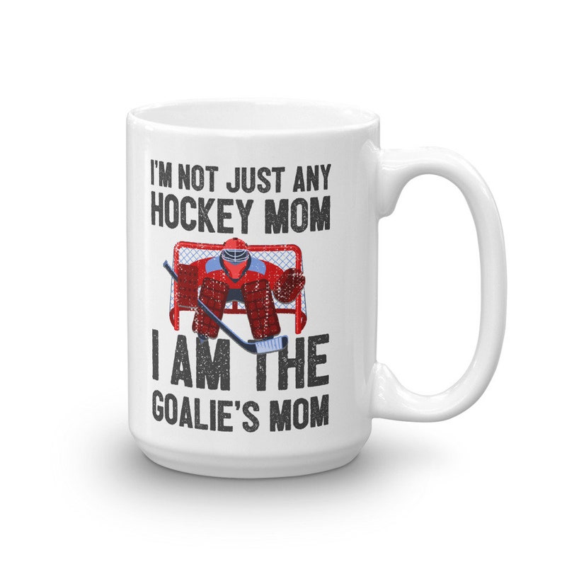 May include: White ceramic coffee mug with a black and white graphic of a hockey goalie in a red and black uniform. The text on the mug reads "I'm not just any hockey mom I am the goalie's mom."