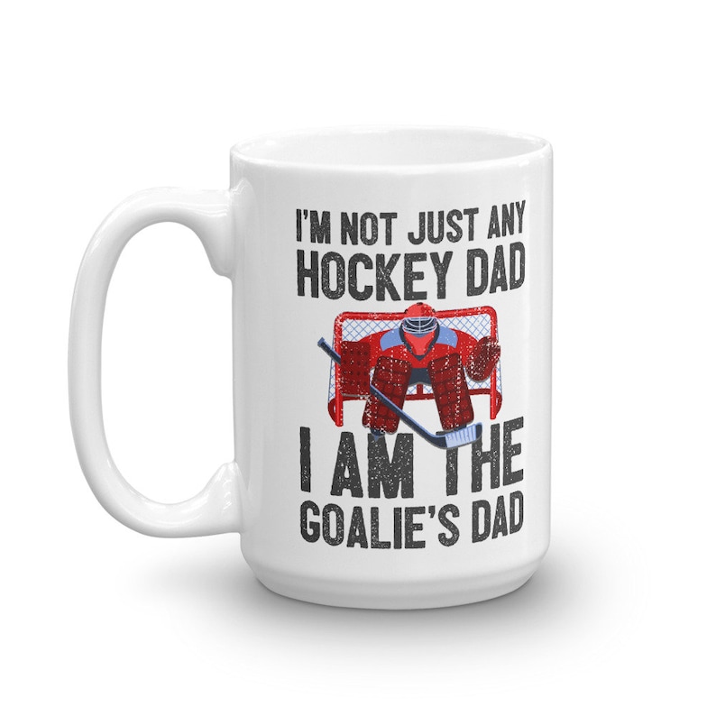 May include: White ceramic coffee mug with a hockey theme. The mug features the text "I'M NOT JUST ANY HOCKEY DAD I AM THE GOALIE'S DAD" in black, along with a graphic of a hockey goalie in red and blue gear.