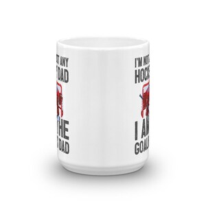 May include: White ceramic mug with the text "I'M NOT ANY HOCKEY DAD, I AM THE GOALIE DAD" in black and red. The mug features a hockey net graphic. A perfect gift for a hockey goalie dad.
