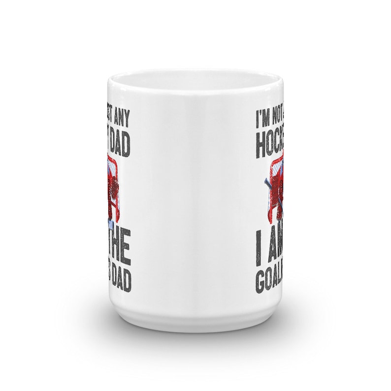 May include: White ceramic mug with the text "I'M NOT ANY HOCKEY DAD, I AM THE GOALIE DAD" in black and red. The mug features a hockey net graphic. A perfect gift for a hockey goalie dad.