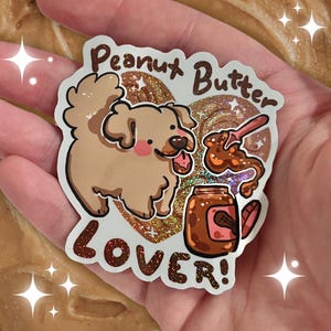May include: A sticker with a cartoon dog, a jar of peanut butter, and a spoon. The text reads "Peanut Butter Lover!" with glitter accents.