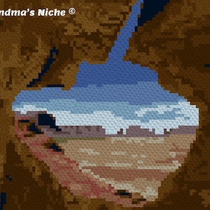 Può includere: Un primo piano di una formazione rocciosa marrone con vista su un paesaggio desertico attraverso un'apertura naturale. Il cielo è blu con nuvole bianche. Il testo "Grandma's Niche ©" è visibile nell'angolo in alto a sinistra.
