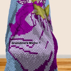 May include: A crocheted baby blanket with a purple angel design. The blanket is light blue with a white border. The angel has a yellow halo and white wings. The text "Grandma's Niche&reg;" is in the lower left corner.