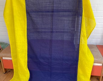 May include: A draped textile featuring a vibrant color block design. The fabric is divided into a central navy blue panel flanked by bright yellow sections. The textile is hanging, showcasing its texture and color contrast.