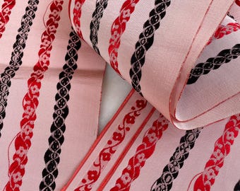 May include: Pink fabric ribbon with black and red velvet stripes. The stripes feature a repeating pattern of woven chains and floral designs.