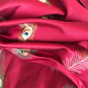 May include: Red fabric with embroidered peacock feathers in shades of green, gold, and blue.