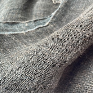 May include: Close-up of a textured, dark green fabric with a loose weave. The fabric appears to be linen or a similar natural fiber, with visible imperfections and a slightly frayed edge. The weave creates a grid-like pattern.