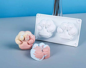 Può includere: Stampo in silicone bianco con due forme di impronta di zampa. Due saponi a forma di impronta di zampa, uno con un vortice rosa chiaro e giallo e l'altro con un vortice rosa chiaro e blu.