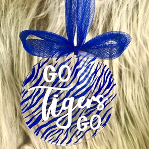 May include: A clear round ornament with a blue and white zebra print design. The ornament has the words "Go Tigers Go" written in white on the front.