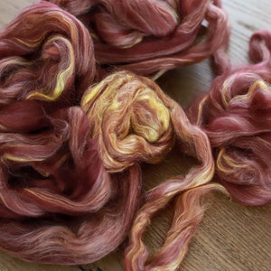 May include: A pile of red and yellow wool roving. The wool is soft and fluffy, and it is perfect for spinning or felting.