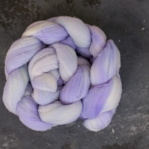 Könnte beinhalten: Ein geflochtenes Bündel aus violetter und weißer Wolle. Die Wolle ist weich und flauschig und perfekt zum Stricken oder Häkeln.