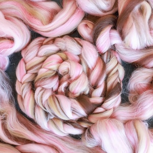 Puede incluir: Primer plano de una trenza de hilo de lana rosa, blanco y marrón. El hilo está dispuesto en espiral, creando un diseño texturizado y colorido.