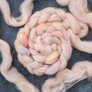 Könnte beinhalten: Nahaufnahme eines geflochtenen Bündels aus weichem, pastellfarbenem rosa, pfirsichfarbenem und gelbem Garn. Das Garn ist spiralförmig angeordnet und erzeugt ein optisch ansprechendes und strukturiertes Design.