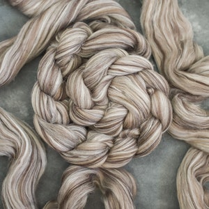 Pode incluir: Um close-up de um feixe de fio marrom e branco trançado. O fio é macio e felpudo, e está disposto em um padrão circular.
