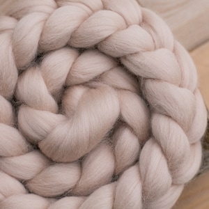 Könnte beinhalten: Nahaufnahme einer großen, geflochtenen Decke aus dickem Strick in einem zarten Rosa. Die Decke besteht aus dickem, flauschigem Garn und ist in einem kreisförmigen Muster angeordnet. Die Textur des Garns ist sichtbar und die Decke wirkt gemütlich und warm.