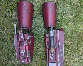 Op de afbeelding: Twee gedemonteerde rode en zilveren Star Wars Mandalorian blaster-rekwisieten. De blasters zijn gemaakt van plastic en hebben een verweerde, verweerde uitstraling.