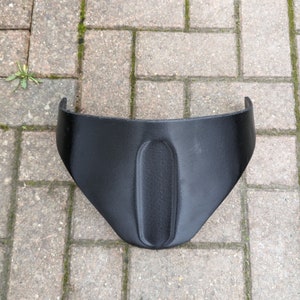 Könnte beinhalten: Schwarzer Motorradkotflügel aus Kunststoff mit einer geschwungenen Form und einer zentralen Öffnung.